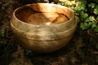Wooden bowl filled with gourds sits on soil surrounded by green plants.