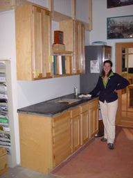Person in kitchen with wooden cabinets, stainless steel countertop, and upper shelving.