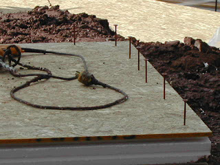 Construction site with mulch pile, metal grates, and rope on concrete ground.