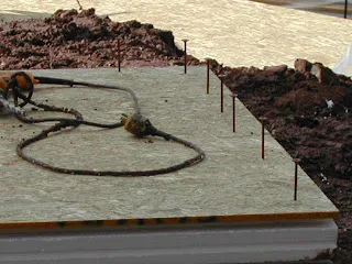 Construction site with mulch pile, metal grates, and rope on concrete ground.