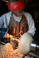 Craftsman in red cap and leather apron woodworking with lathe tools at night