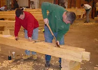 Two woodworkers in colorful clothing working on a large wooden board in workshop
