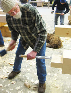 Older man in plaid shirt using sledgehammer to break brick, construction work scene