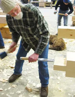 Older man in plaid shirt using sledgehammer to break brick, construction work scene