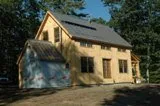 Yellow cottage house with gable roof surrounded by green trees and blue sky