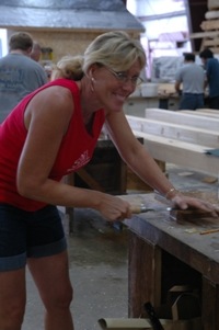 Woman in red tank top working with woodworking tools at workbench in workshop.