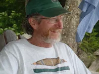 Man in green cap and fish t-shirt standing outdoors smiling
