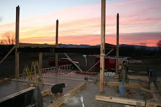 Construction site with wooden posts and structural framework at sunset with pink sky
