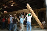 Group of people lifting and holding large wooden beam together indoors