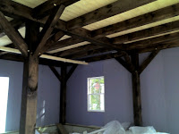 Rustic wooden beam ceiling structure with white walls and natural light from window