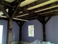 Rustic wooden beam ceiling structure with white walls and natural light from window