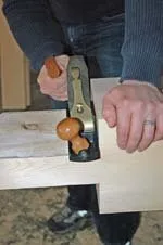Person holding vintage tool with wooden handle and metal components on white surface