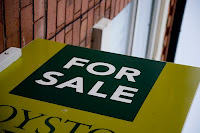 A green and black "FOR SALE" sign displayed on a doormat outside a house entrance.