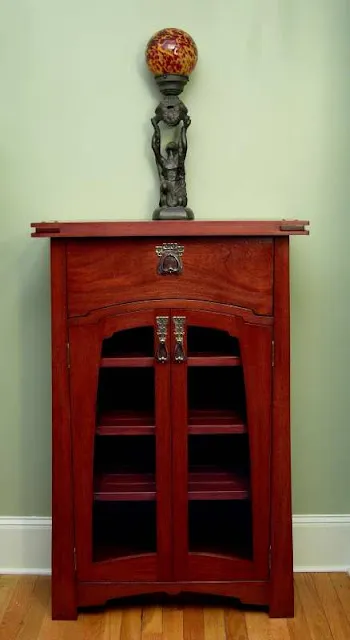 Red wooden cabinet with glass doors and decorative statue with red ball on top.