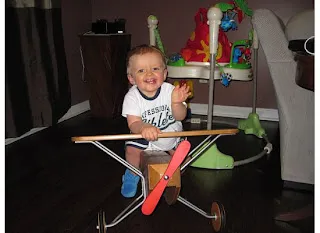 Young child sitting in a red toy airplane in an indoor room with Christmas decorations.