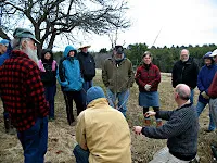 Group of people gathered outdoors in winter clothing planting or tending to a young tree