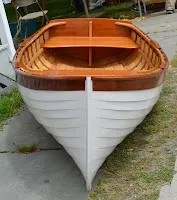 Wooden and white rowboat viewed from above, displayed on pavement outdoors