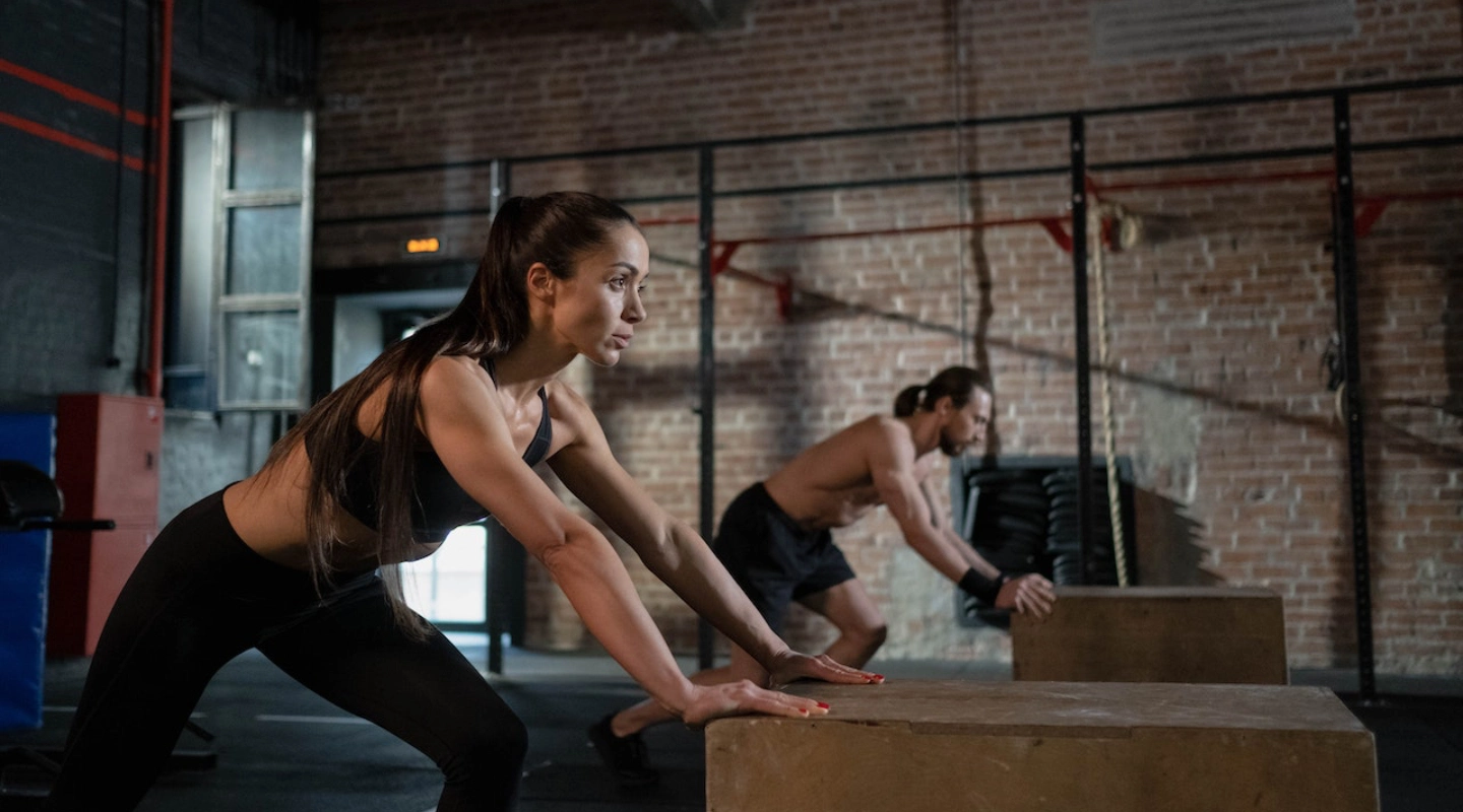 A man and woman perform push-ups on a box at CrossFit 812 in Vincennes, IN, showcasing their fitness routine.