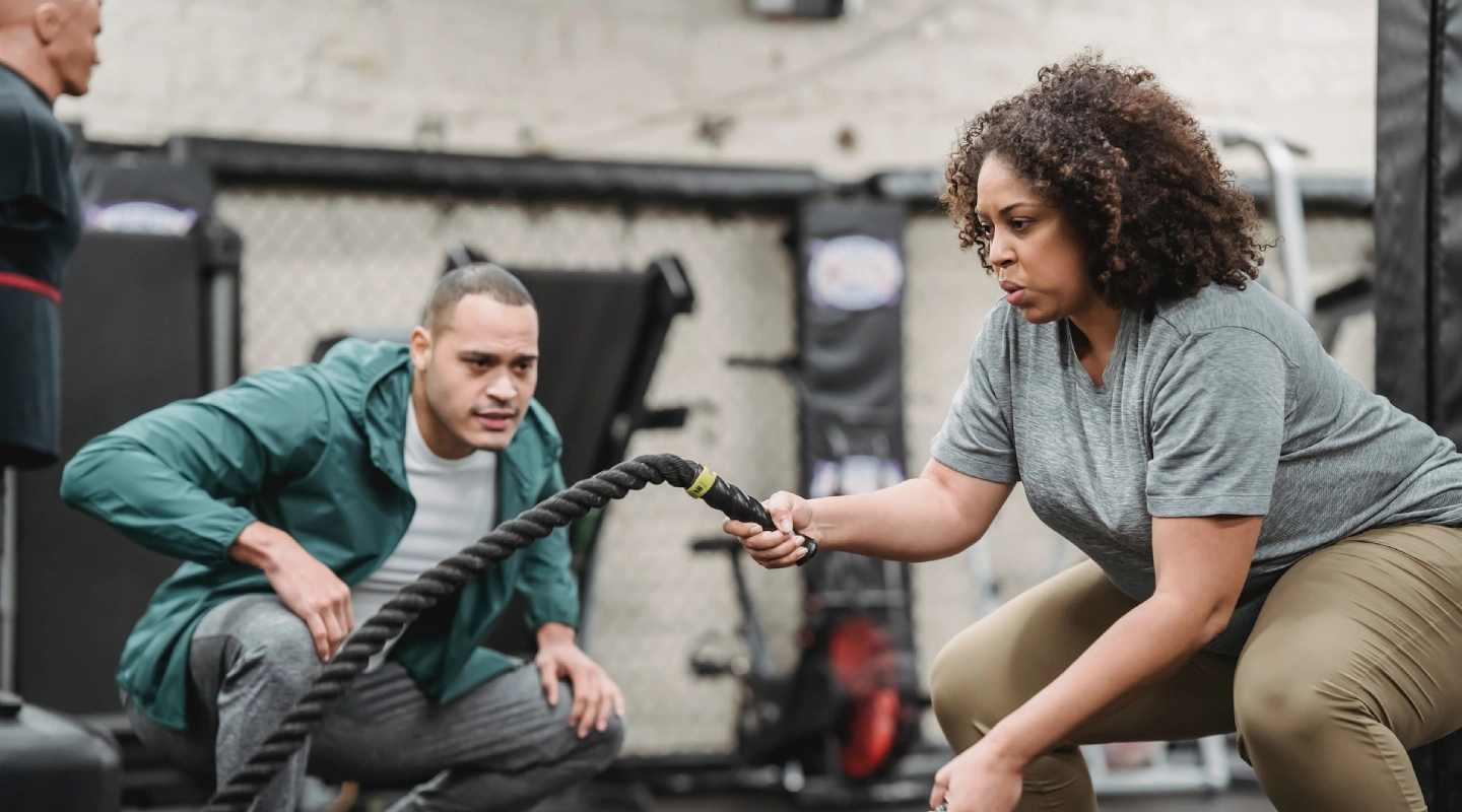 A woman holds a rope while a man stands beside her, both participating in a personal training session at CrossFit 812.