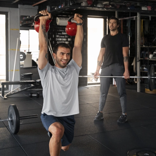 A man lifts a kettlebell in a gym at CrossFit 812 in Vincennes, IN, showcasing strength and fitness training.
