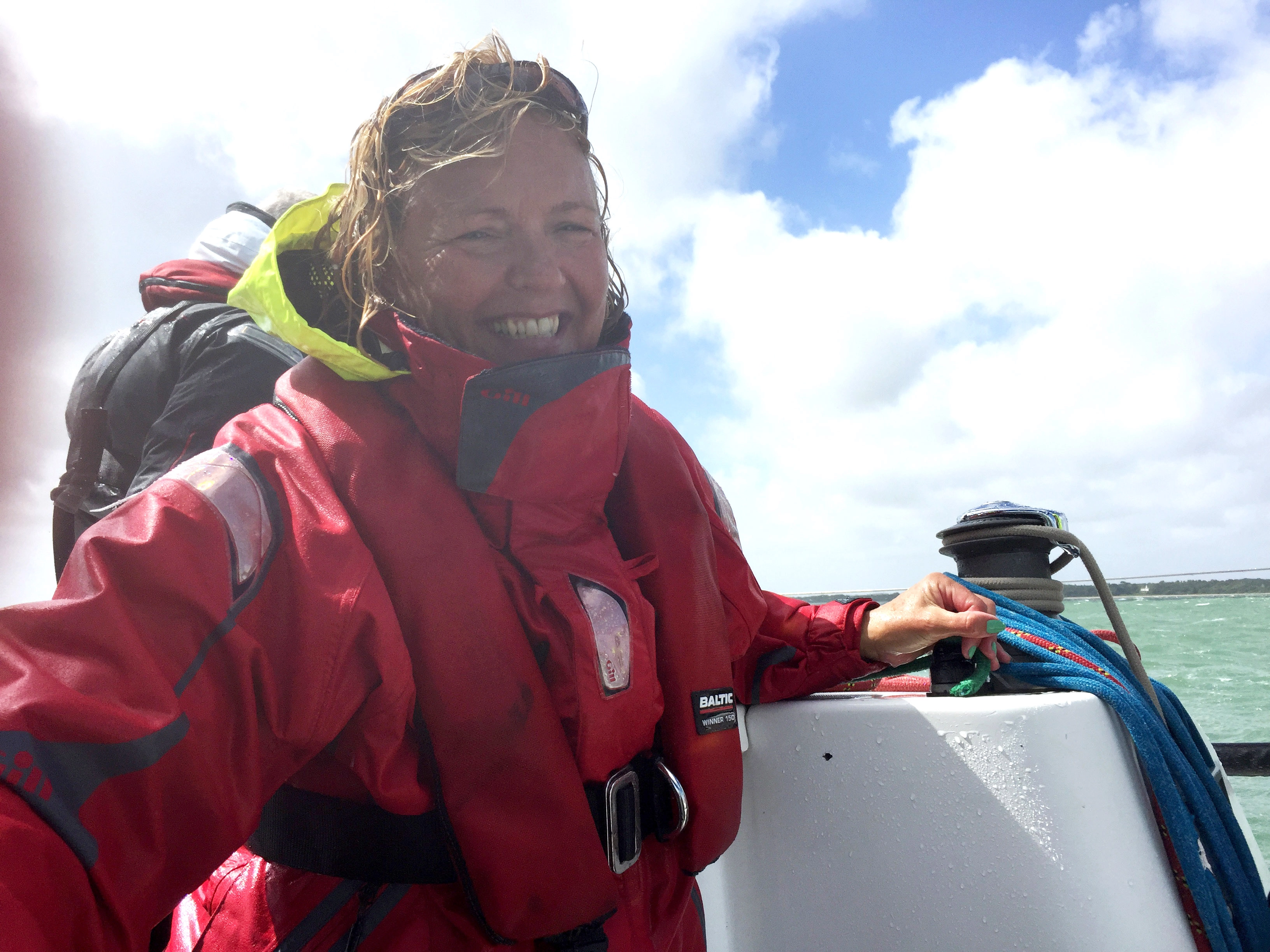 Smiling woman in a red waterproof jacket and life vest on a boat with blue rope and water in the background.