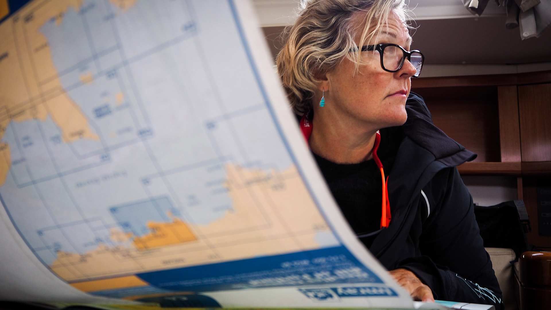 Woman with glasses studying a nautical chart inside a boat cabin.