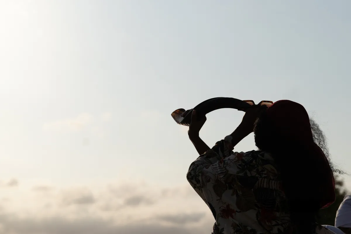 A lady blowing a shofar (Trumpet) towards the sky.