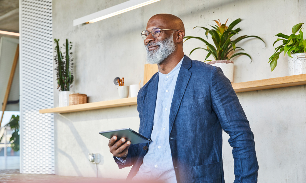 Smiling man looking away while holding digital tablet standing at work
