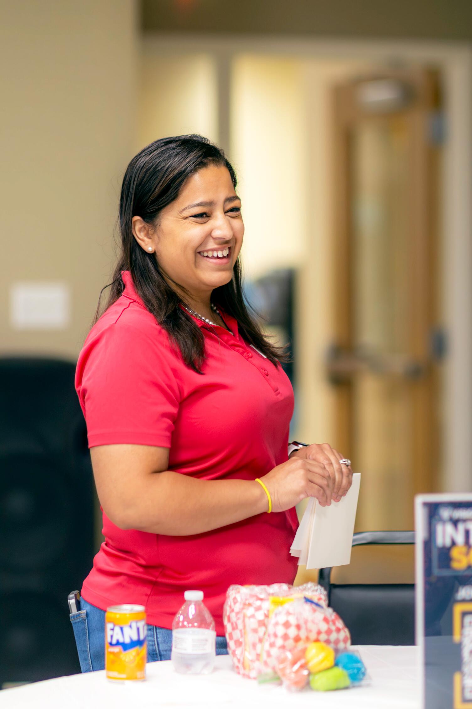 A woman wearing a red shirt, smiling in front of a table