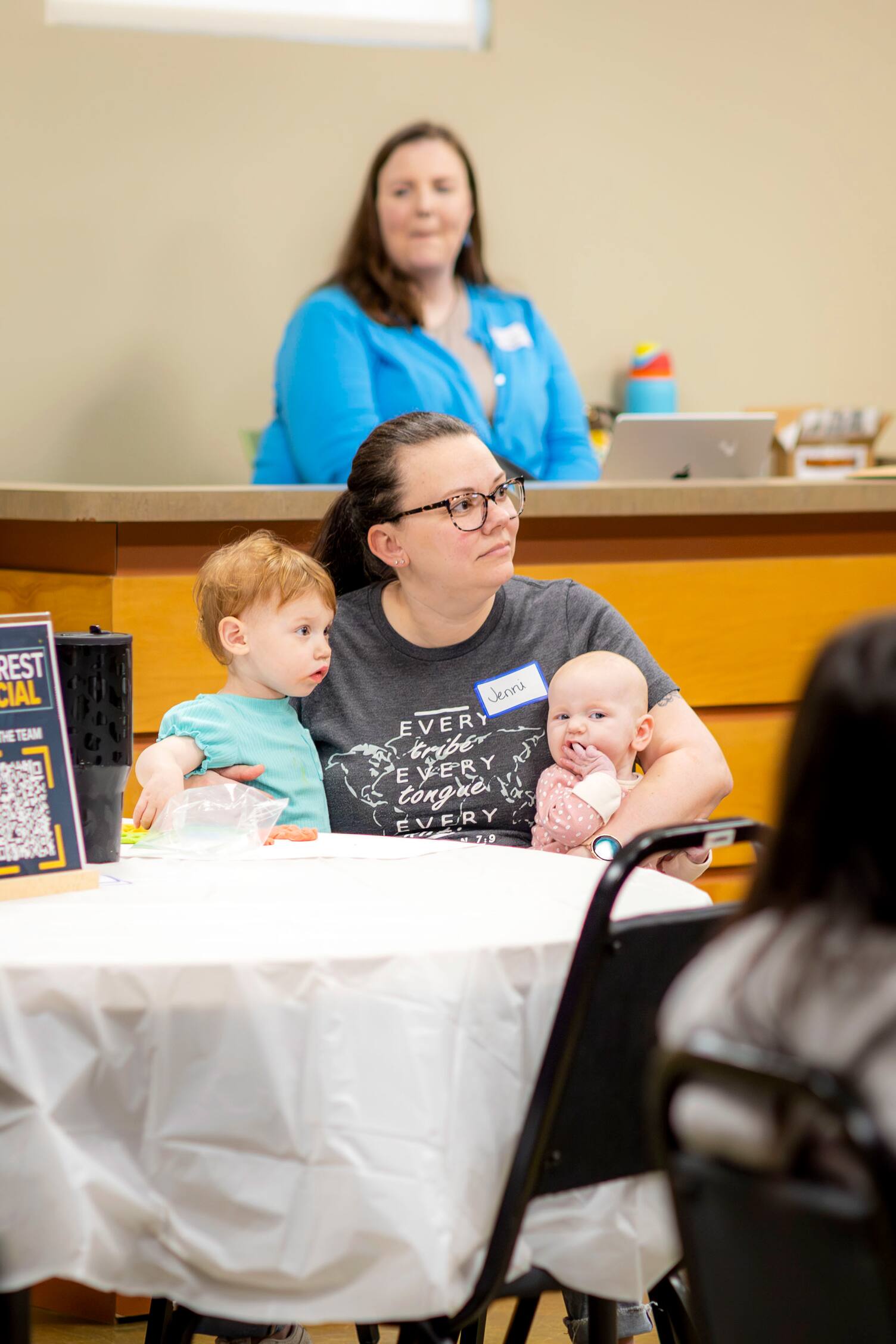 A mother sitting at a table holding her two children
