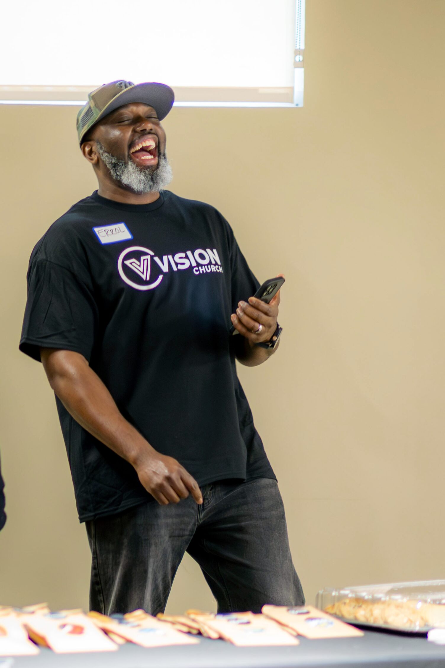 A guy wearing a Vision Church shirt laughing at his phone