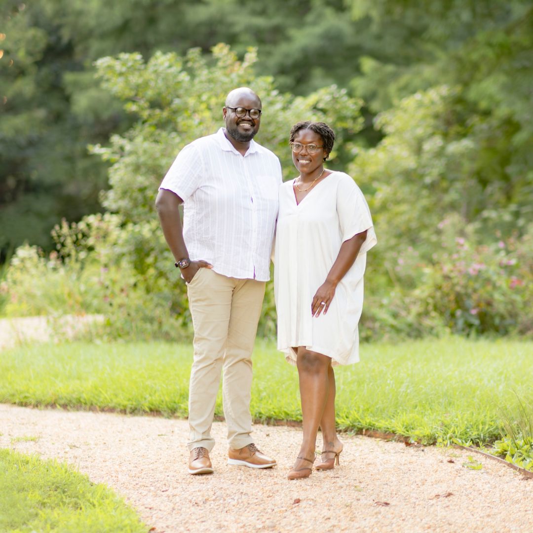 A husband and wife holding their son and daughter with grass and trees in the background.