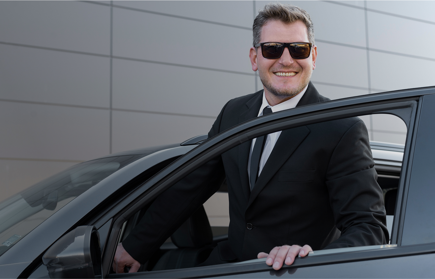 Man in suit standing by black car