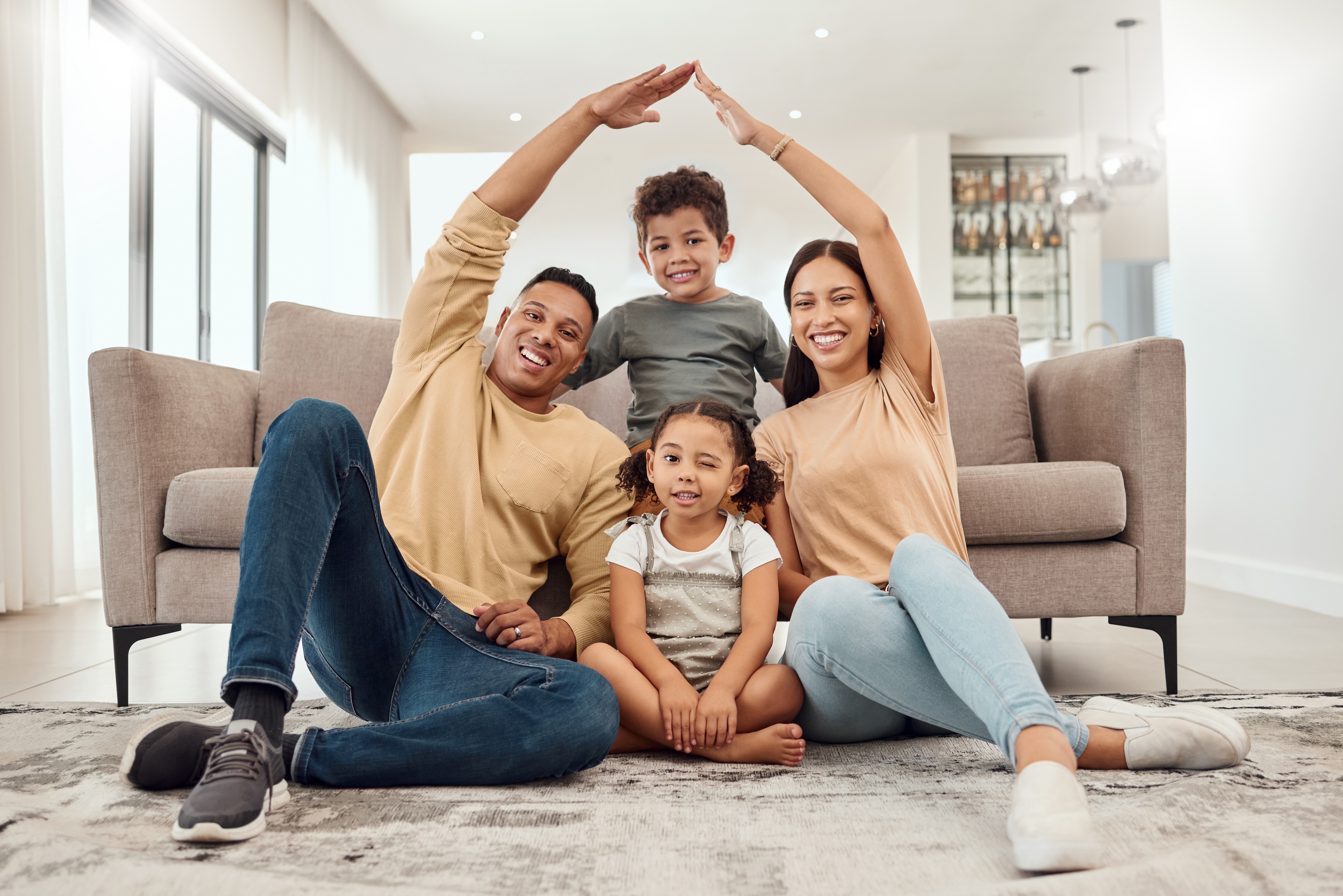 Happy family of four, with parents making a "roof" gesture over their children, symbolizing home and comfort at Canvas at Prairie Center in Brighton, CO.
