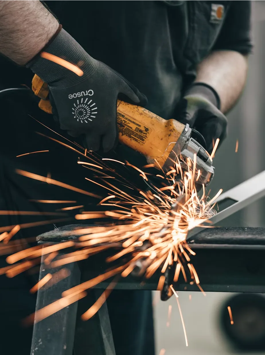 Close-up of a technician wearing Crusoe-branded gloves using an angle grinder to shape a metal bracket for a GPU cluster.