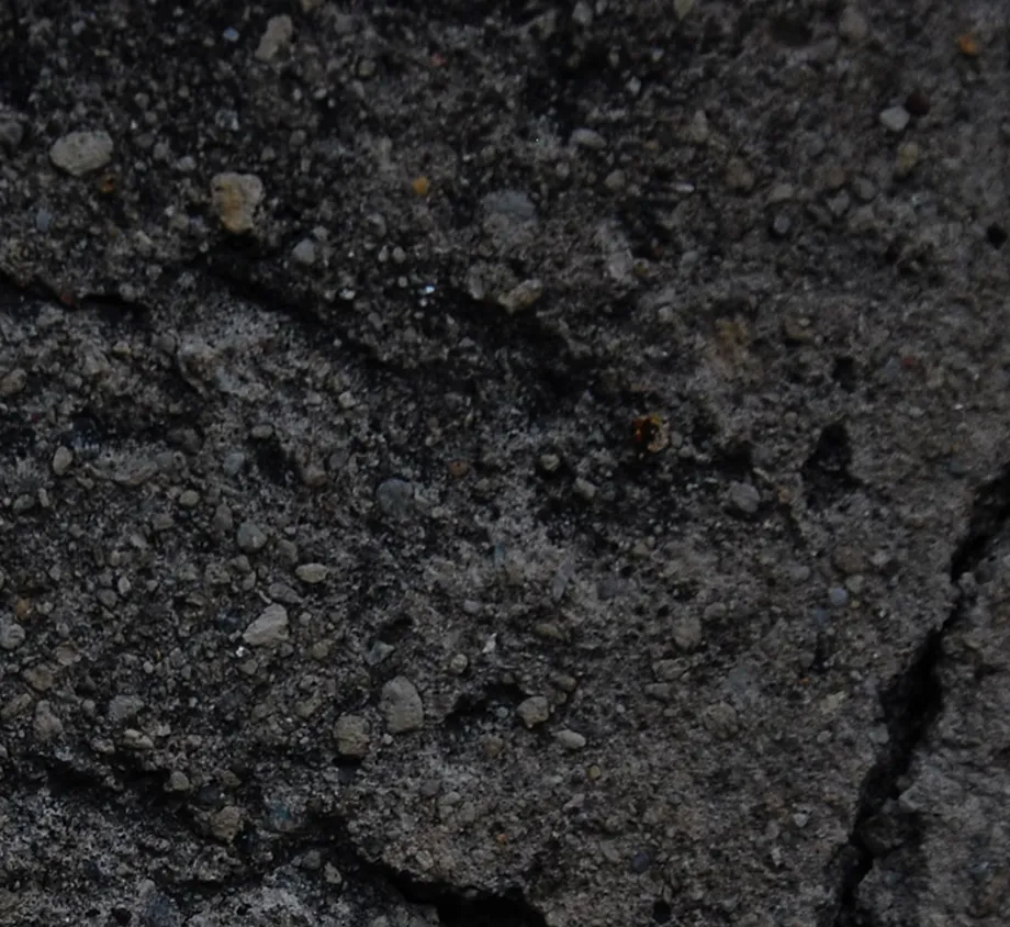 A close-up, macro view of a dark, rough surface of coal, showing its natural texture, cracks, and mineral composition.