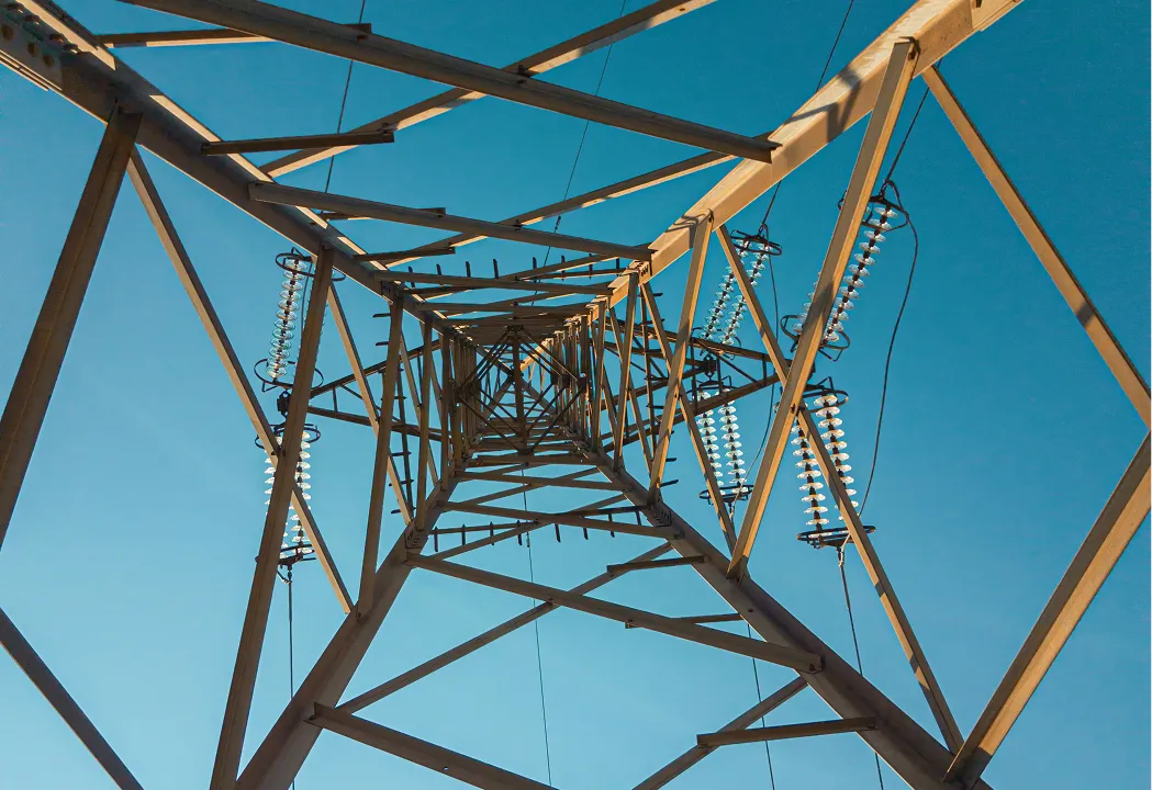 A low-angle, upward view through the intricate steel lattice of an electrical transmission tower.