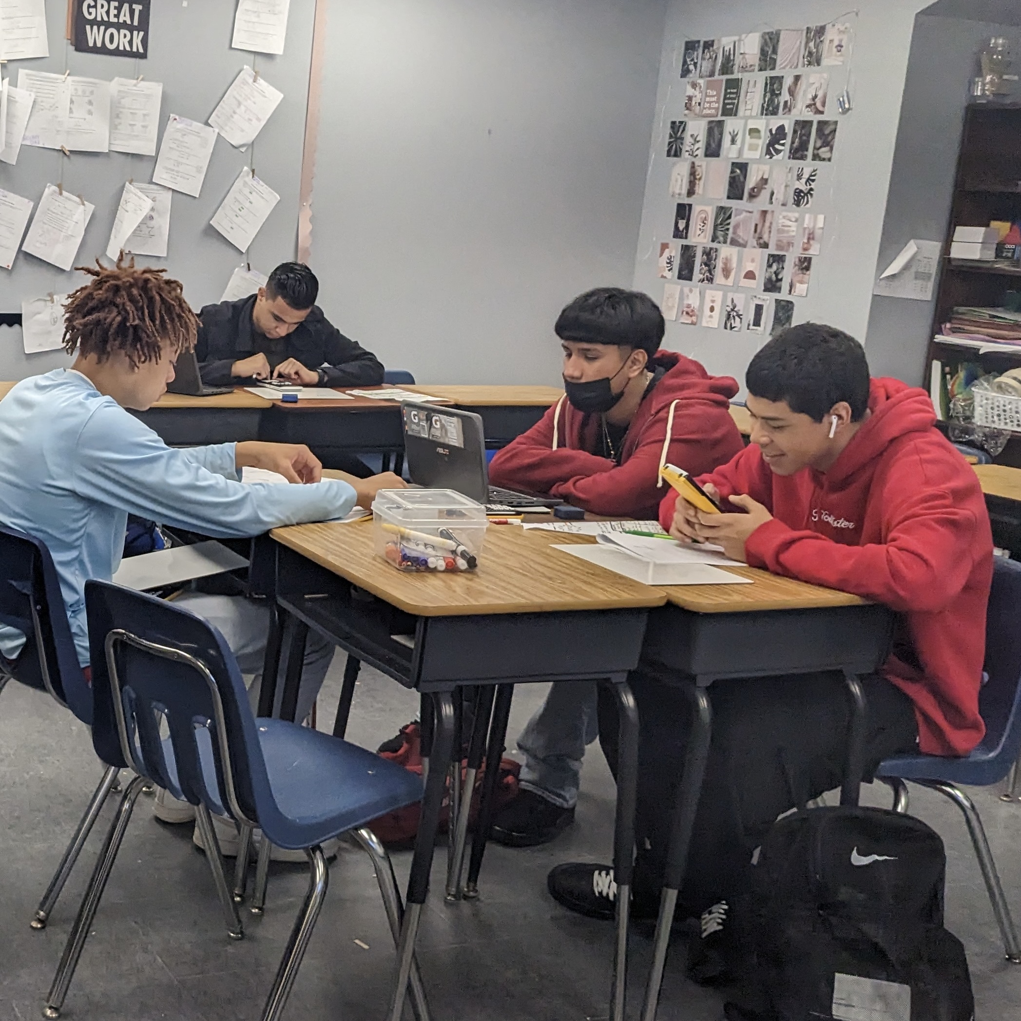 A photo of Lidia's classroom shows 4 boys using chromebooks, graphing calculators, and white boards to do classwork.