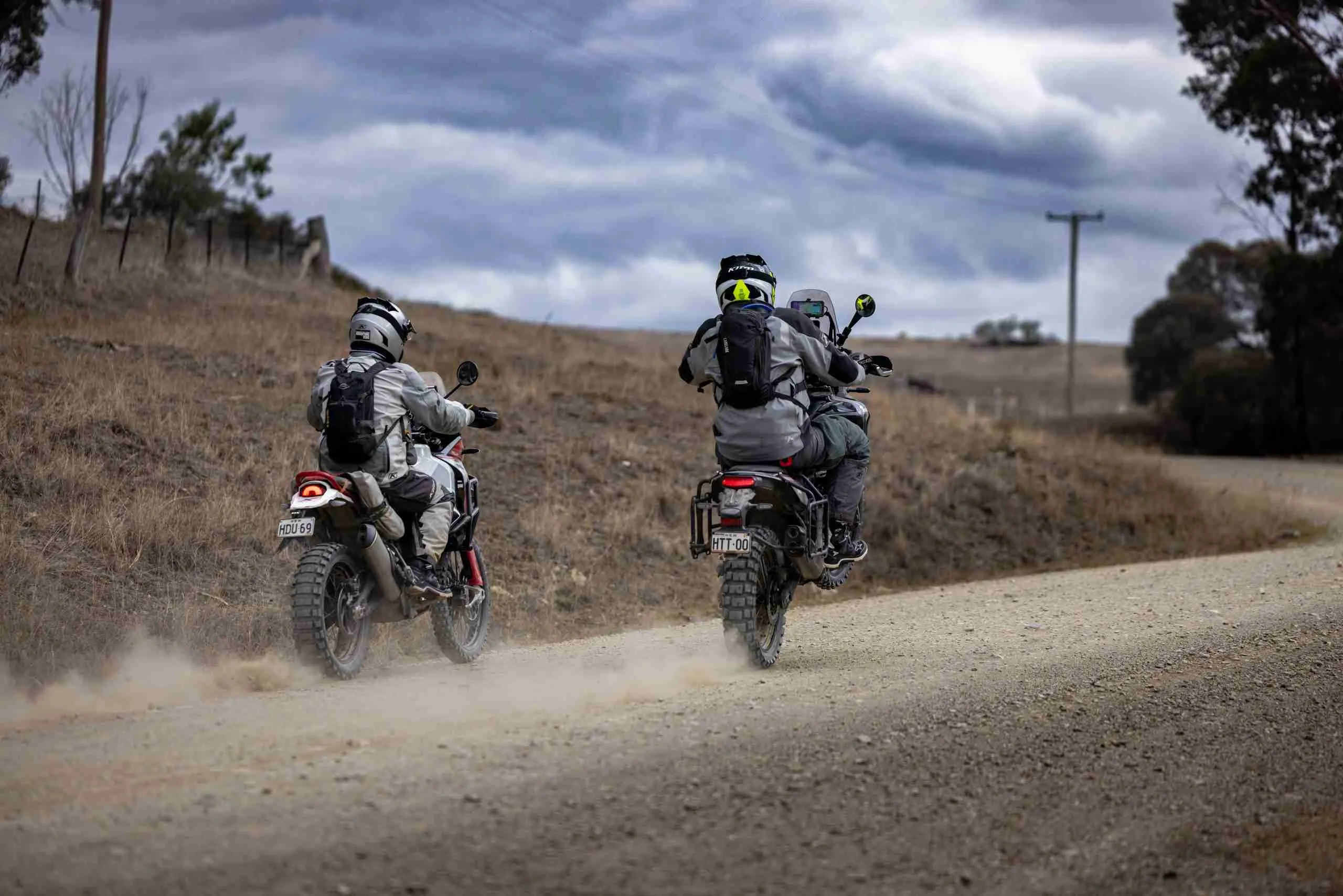 two motorcycle riders riding along a dirt road