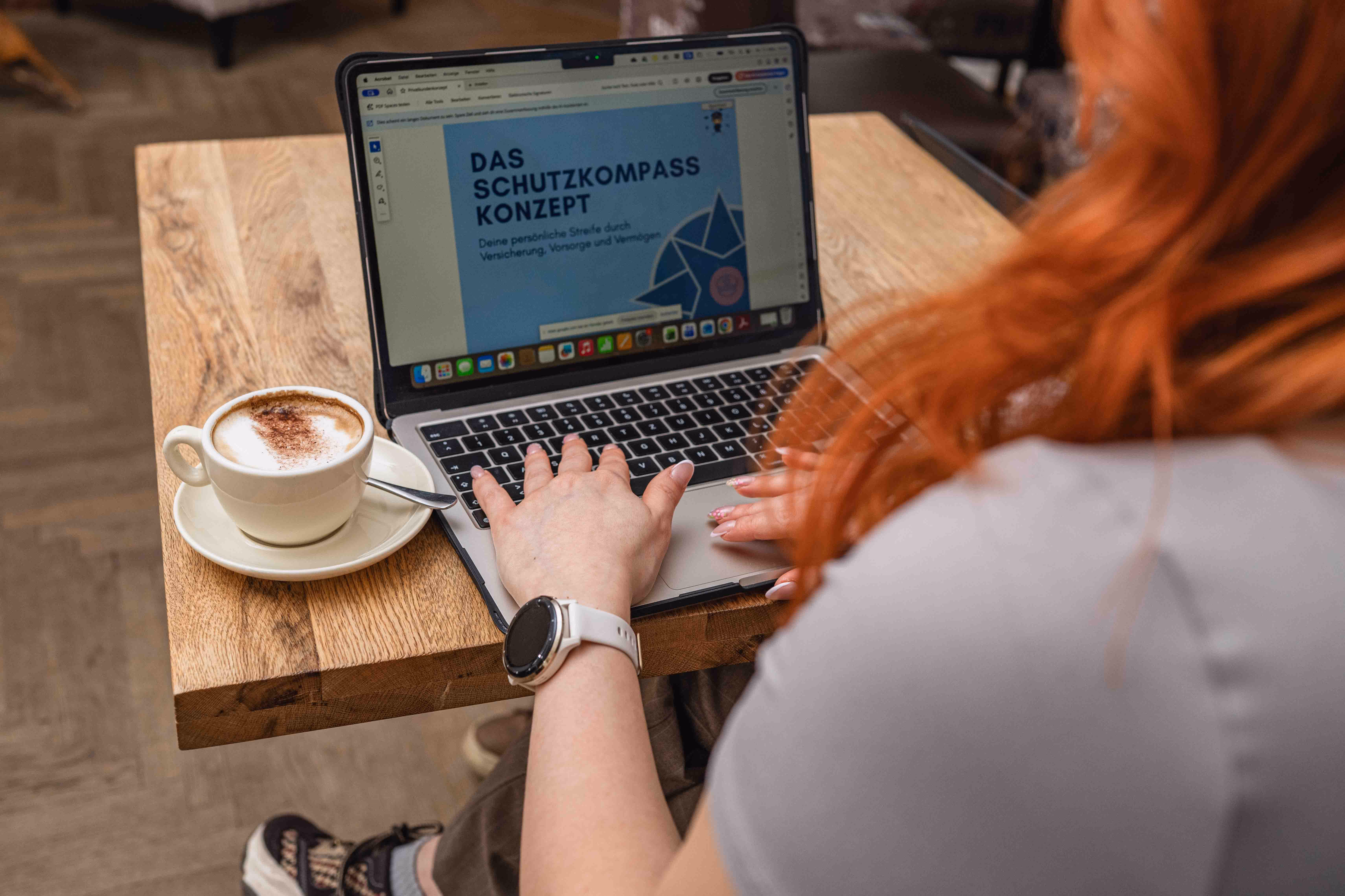 Laptop-Bildschirm zeigt das Schutzkompass-Konzept, Jennifers Hand tippt, Kaffee steht daneben