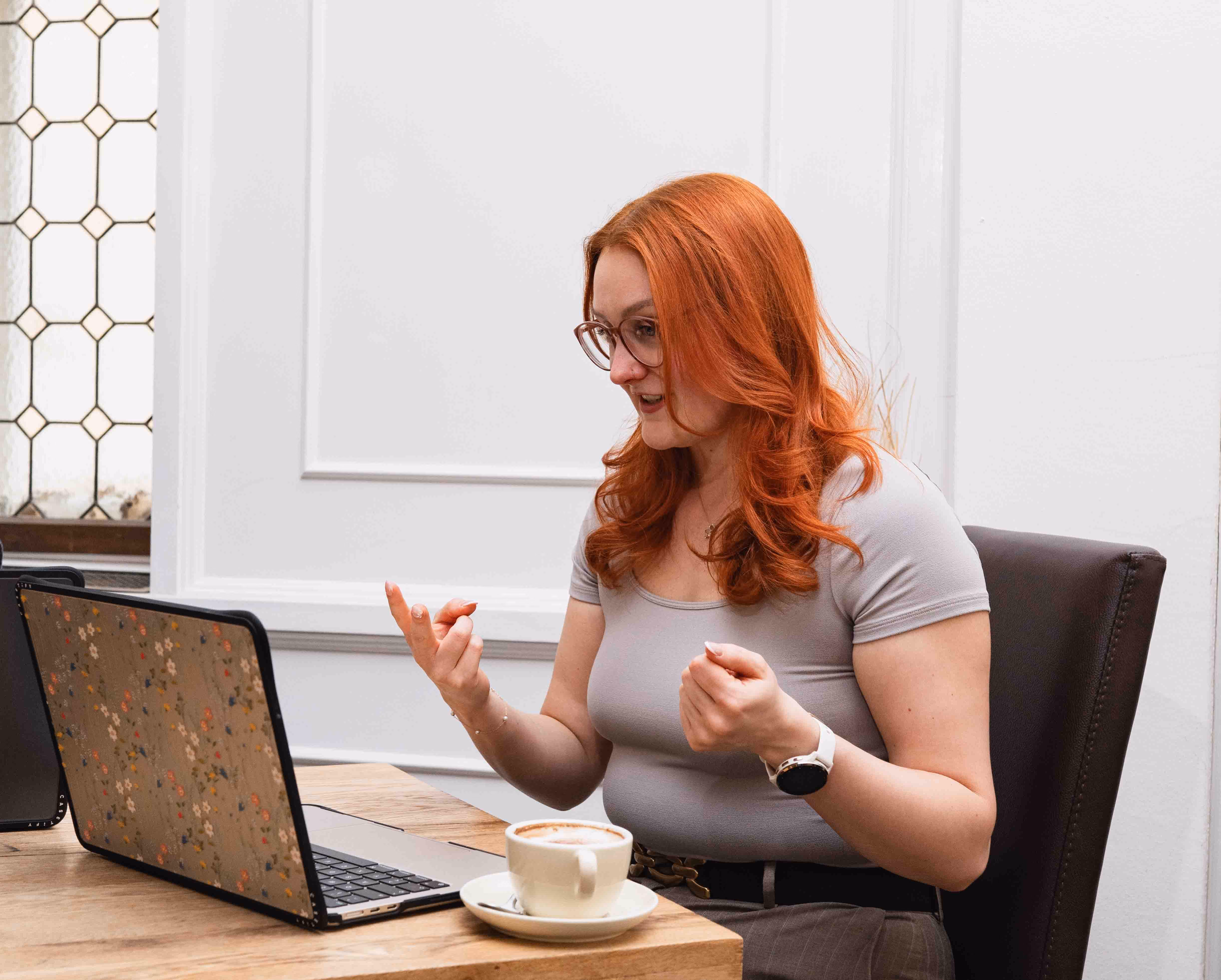 Jennifer im Video-Call mit einer Kundin, Laptop und Kaffee am Tisch