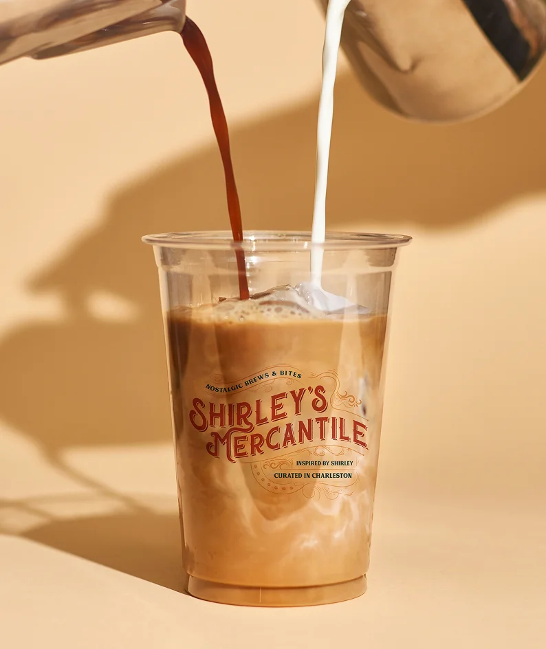 Fresh coffee being poured into a Shirley’s Mercantile branded cup, highlighting the brand’s warm, artisanal atmosphere