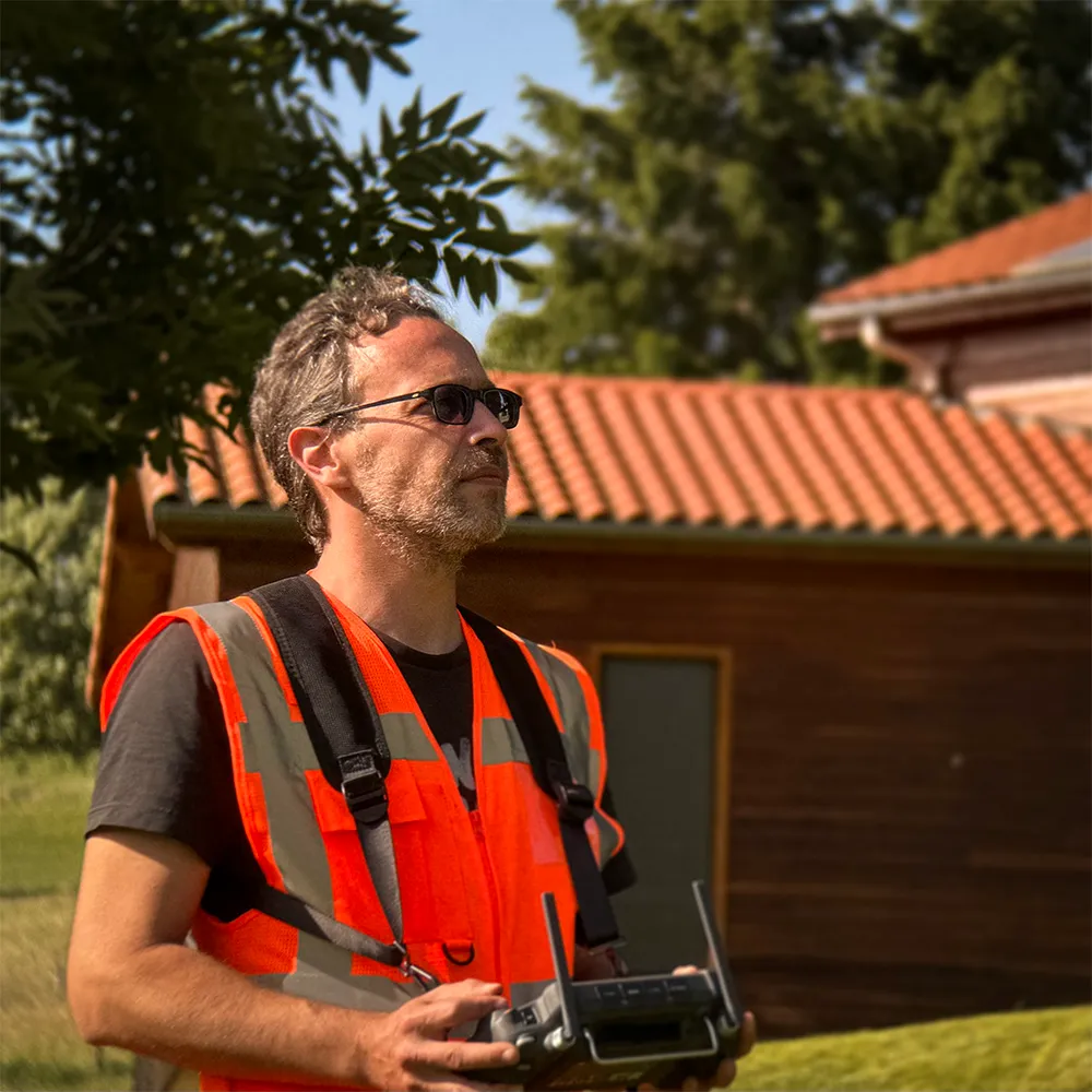 David DHALLU de profil pilotant un drone de nettoyage devant une toiture de maison