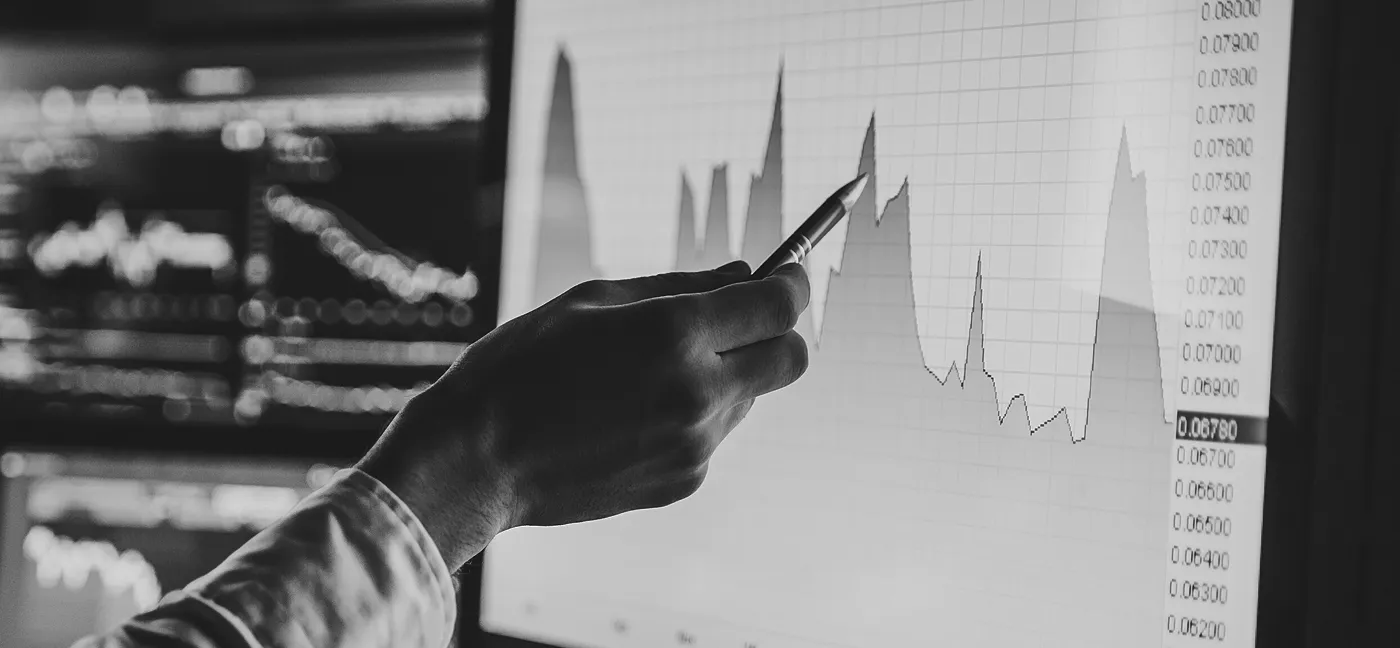 Hand holding a pen pointing at a data chart displayed on a computer screen.
