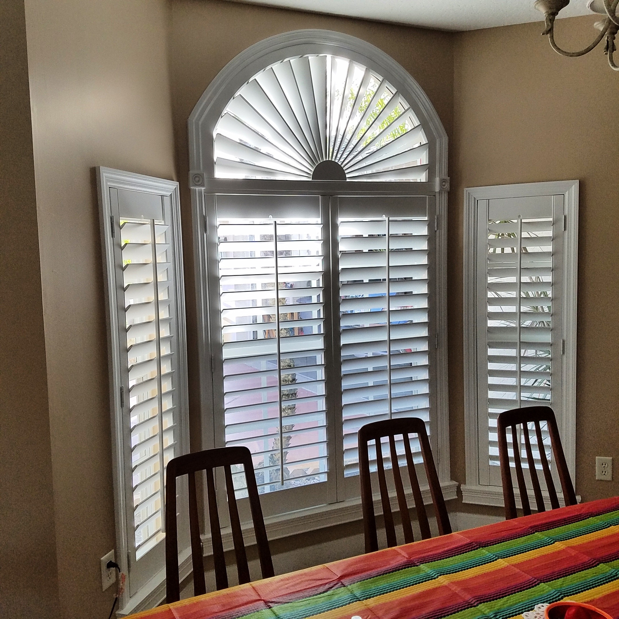 White sunburst plantation shutter following an arched window above matching rectangular shutters