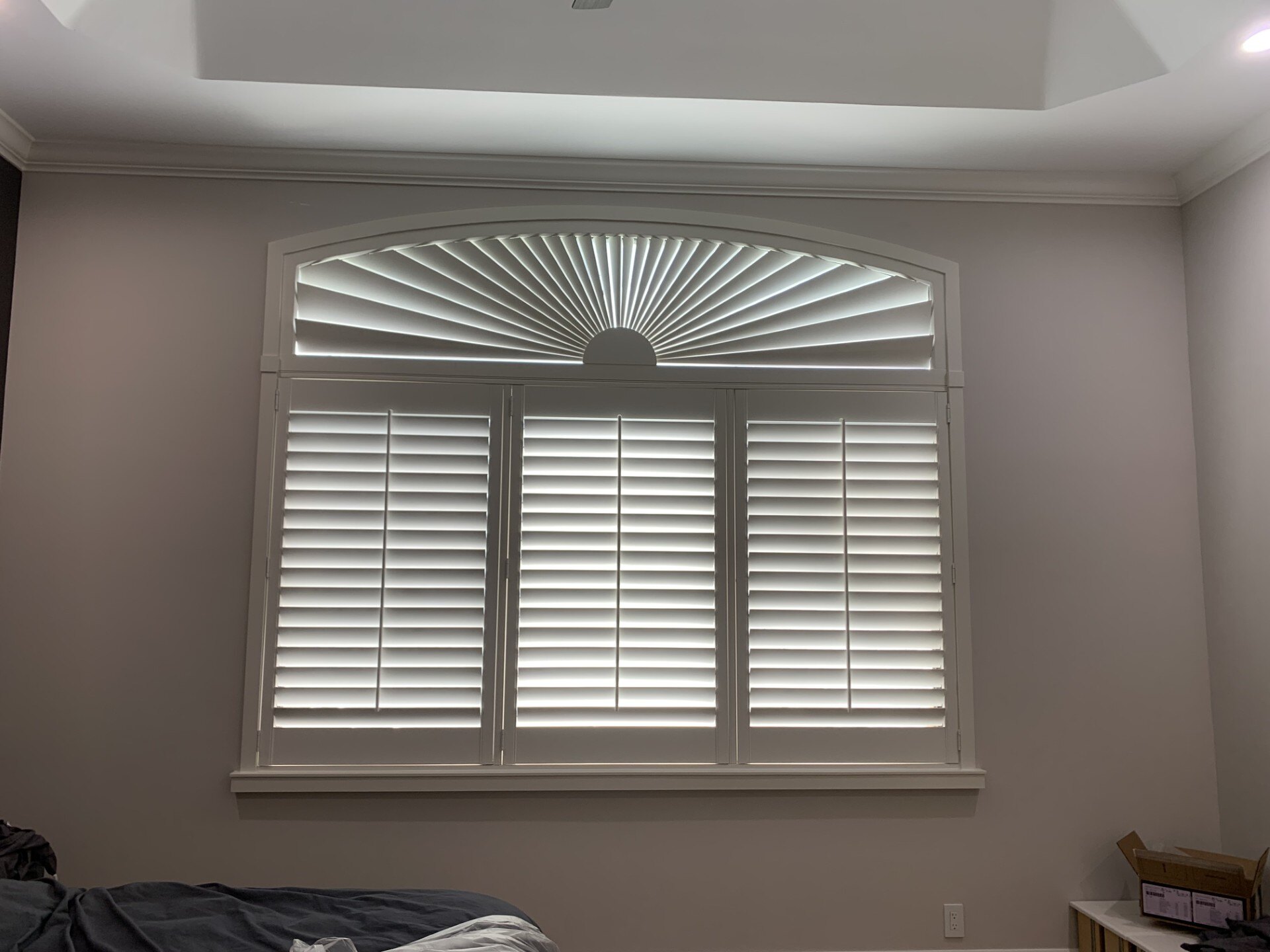 Wide eyebrow arch sunburst shutter with fan-shaped louvers over bedroom plantation shutters