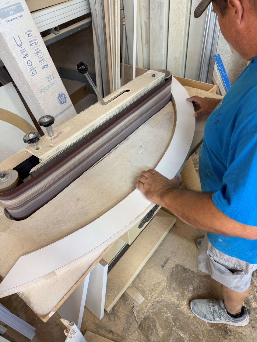 Craftsman sanding the inner curve of a custom hardwood sunburst shutter frame in Palm City