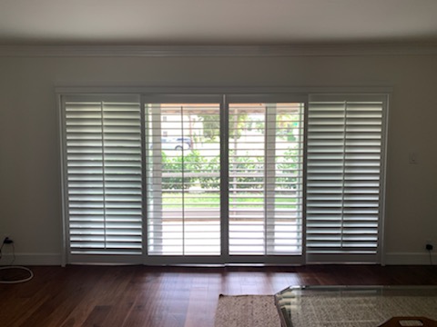 Four broad white shutter faces across a living-room glass-door opening