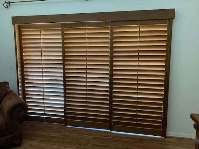 Three broad stained shutter faces across a wide opening above a plank-pattern floor