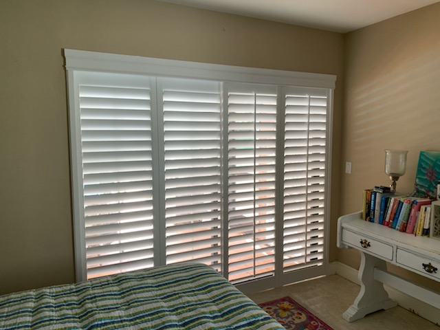 Four narrow white shutter leaves covering a bedroom glass-door opening